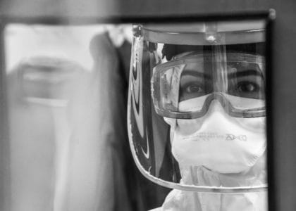 A healthcare worker in full PPE looking through a glass door with an overwhelmed expression.